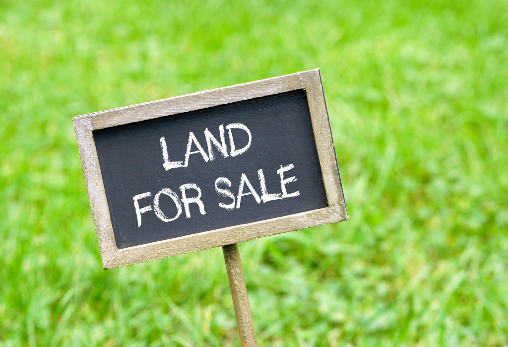 wooden sign with land for sale in chalk staked on a green field